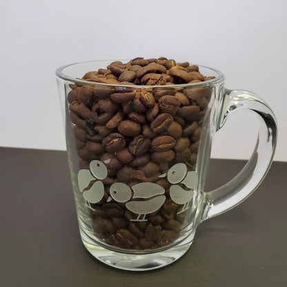 idioma roastary Clear, glass mug, logo on 2 sides with bean bird at bottom of mug.  Coffee sold separately. back side of mug full of beans